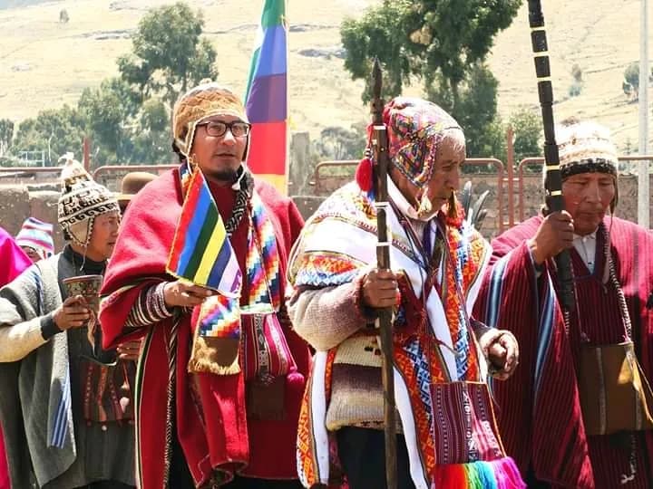 Andean authorities holding staffs of office beside the wiphala flag
