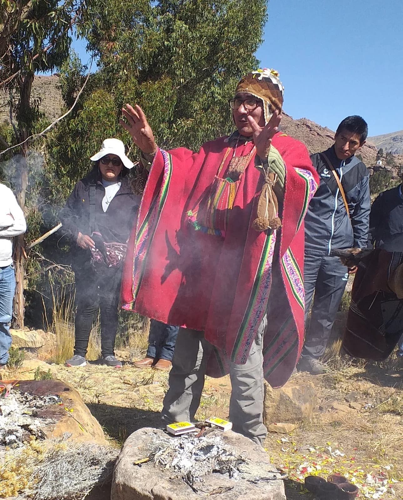 Andean spiritual guide in a red poncho blessing amid the smoke of an offering