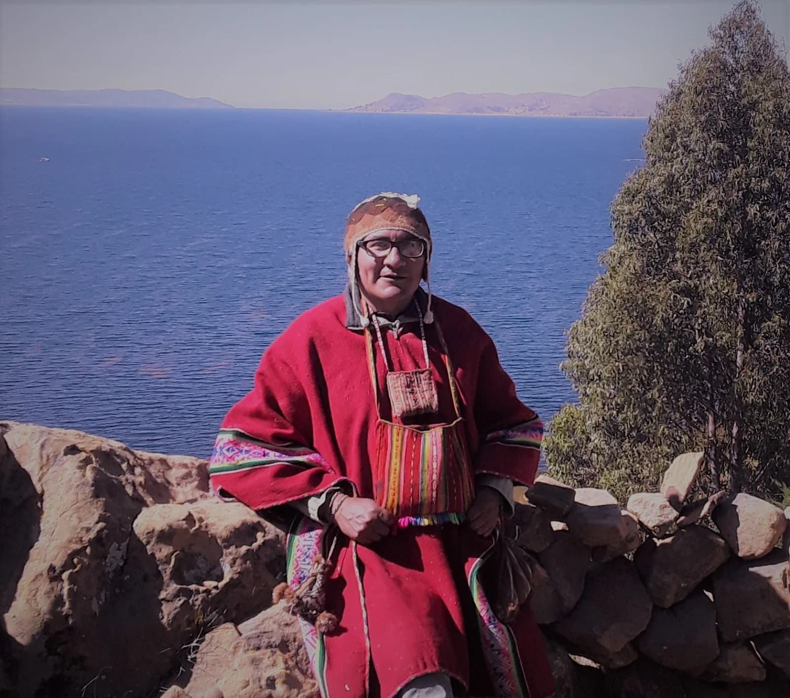 Andean guide in a red poncho before the waters of Lake Titicaca