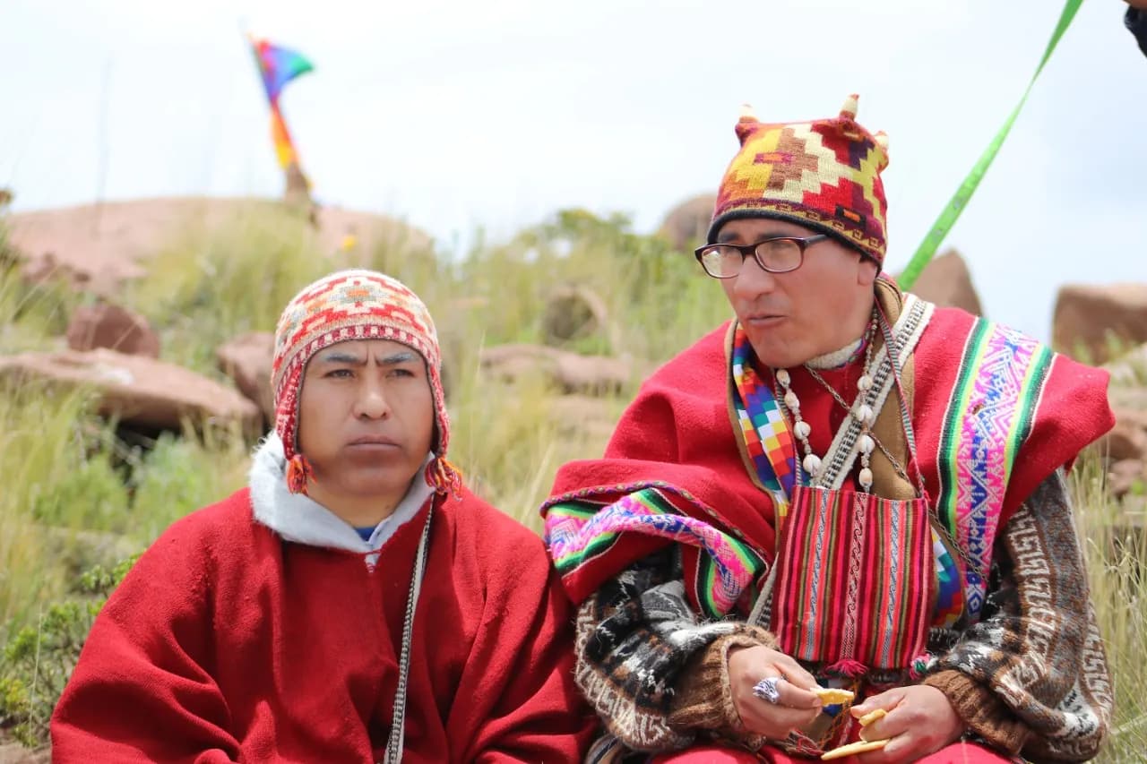 Two Andean masters in red ponchos and chullos during a ceremony