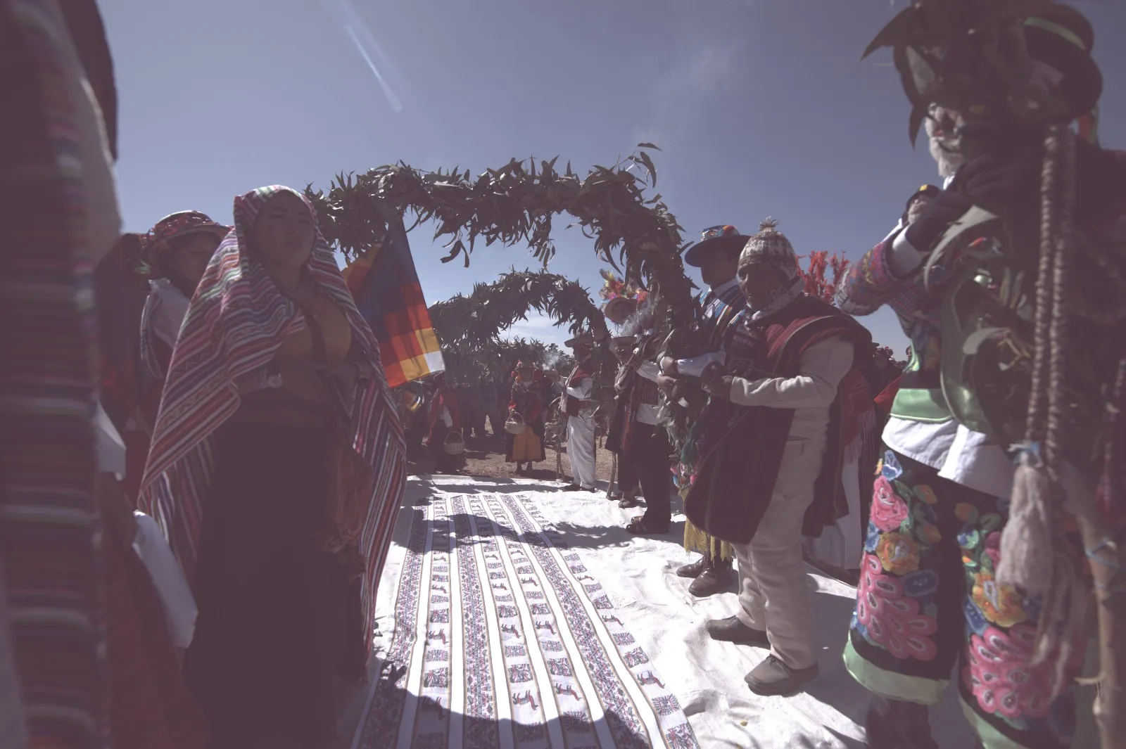 Andean wedding under an arch of leaves, with wiphala and ceremonial textiles
