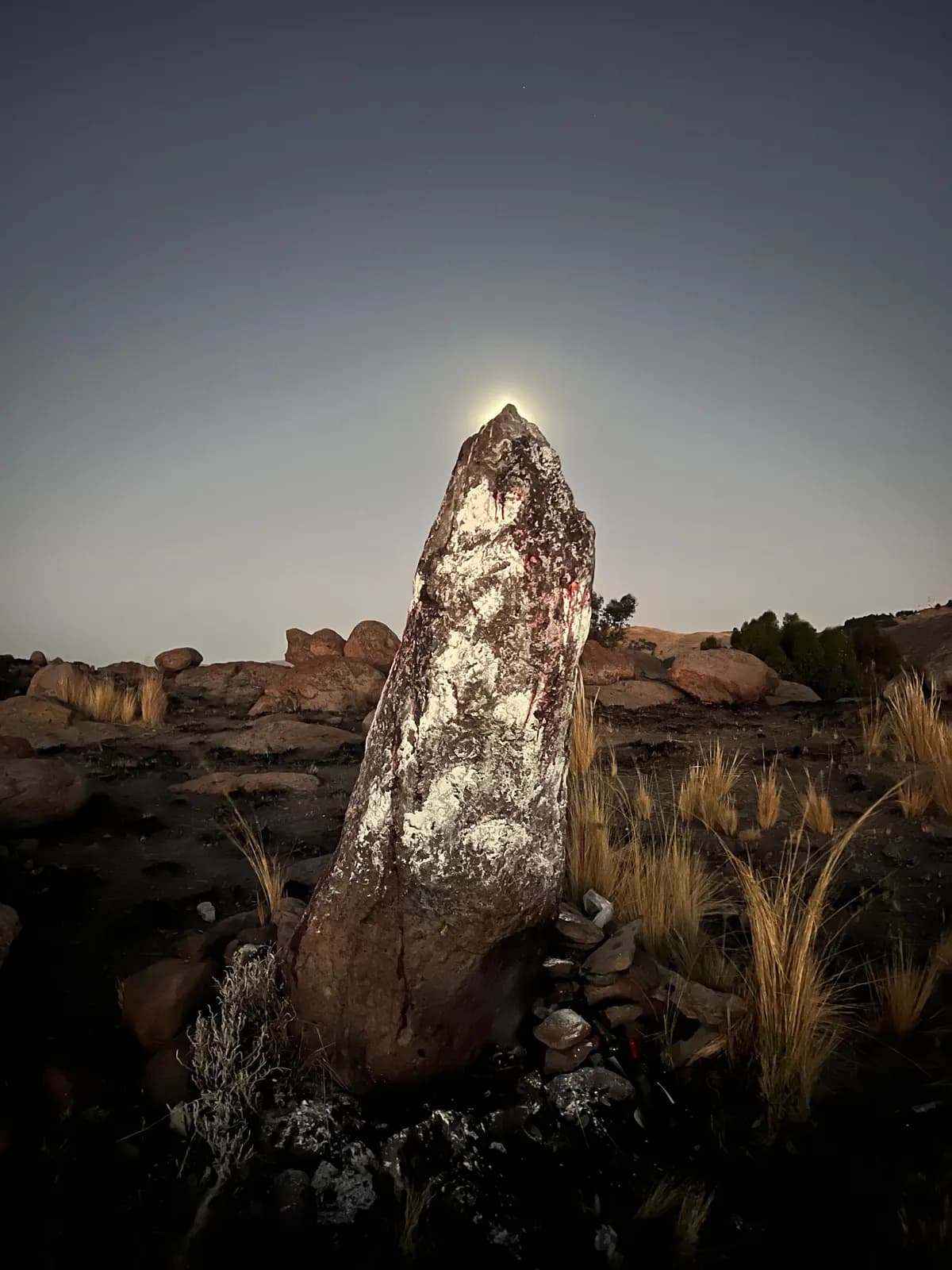 Wanka, a sacred Andean standing stone, with the sun rising behind its peak on the altiplano